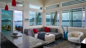 A modern living room with a large window, a ceiling fan, and a view of the sea. - Private Oceanfront Villa for 2 | Plunge Pool | St. John USVI (St. John)
