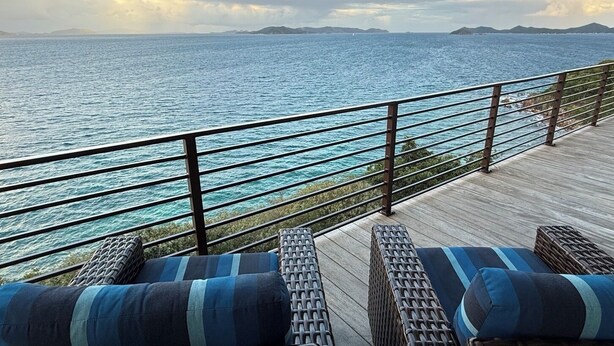 A deck with wicker furniture and cushions, overlooking a body of water with distant land. - Private Oceanfront Villa for 2 | Plunge Pool | St. John USVI (St. John)