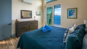 A bedroom with a bed, a dresser, a mirror, and a view of the sea through a sliding door. - Private Oceanfront Villa for 2 | Plunge Pool | St. John USVI (St. John)