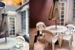 En terrasse med et rundt bord, hvide stole, en parasol og en træterrasse.