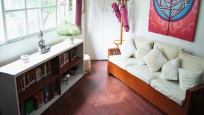 A cozy living room with a wooden sofa, a bookshelf filled with books, a small Buddha statue, and a colorful abstract painting on the wall. - Loft & Terrace Central, Safe, Condesa/Roma/WTC, kitchenette, Hi-Wifi, Get to know us (Ciudad de México)