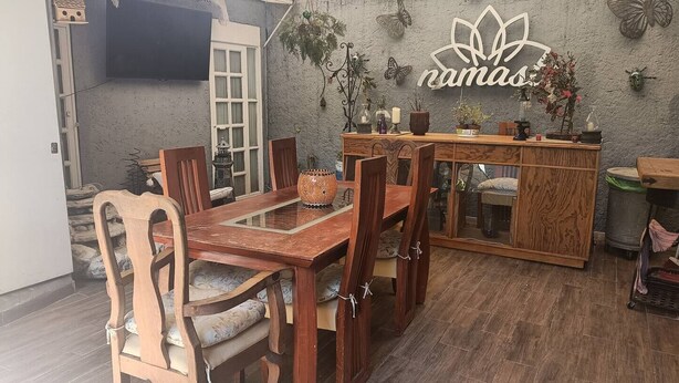 A dining area with a wooden table and chairs, a cabinet with glass doors, and a wall-mounted sign reading "namas". - Loft & Terrace Central, Safe, Condesa/Roma/WTC, kitchenette, Hi-Wifi, Get to know us (Ciudad de México)