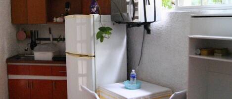 A compact kitchen with a refrigerator, a microwave, a sink, and a small table with a water bottle.