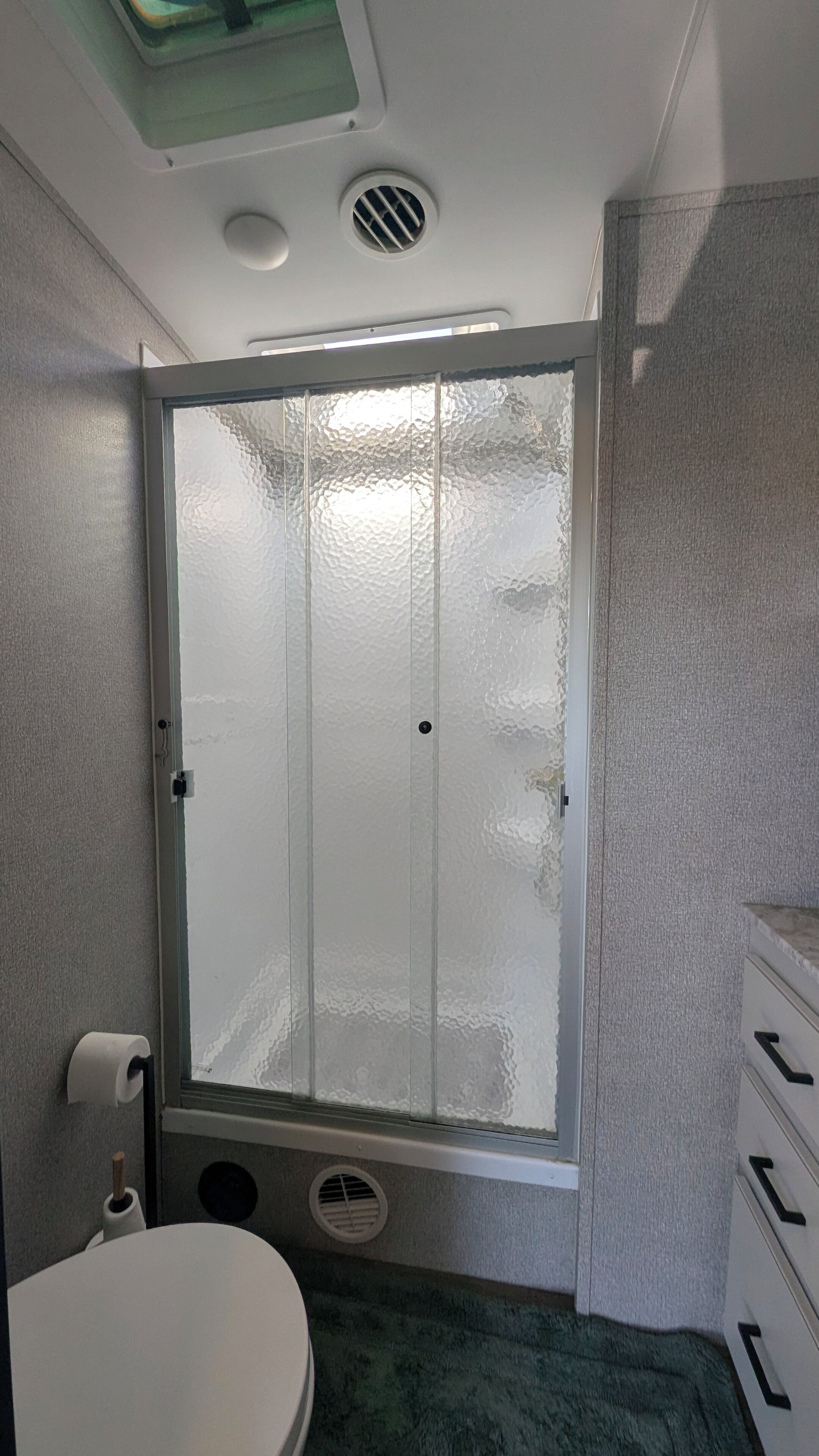 Een badkamer met toilet, een douchecabine met ruitverdeling en een wastafel met handdoekdispenser.