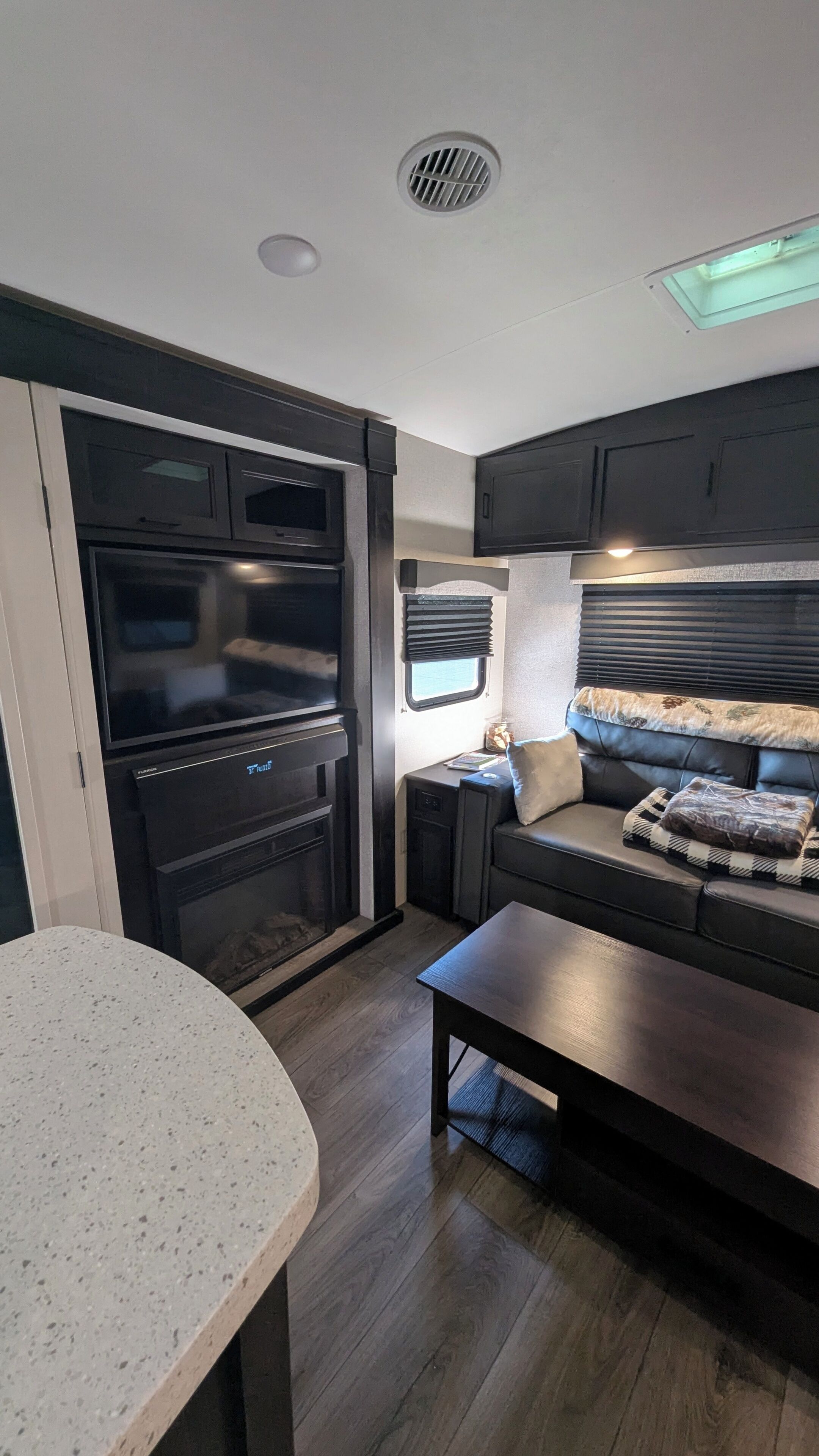 A compact RV interior with a kitchenette, a seating area with a sofa and a table, and a small window.