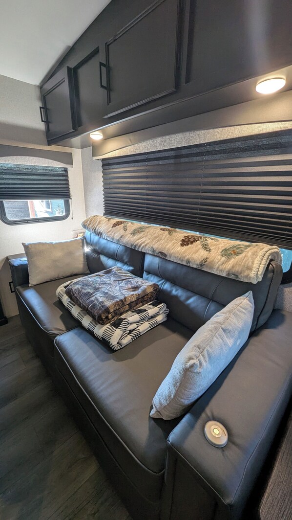 A cozy RV interior with a sectional sofa, a small table, and a window with blinds. - RV Retreat on Green Thumb urban farm (Puyallup)