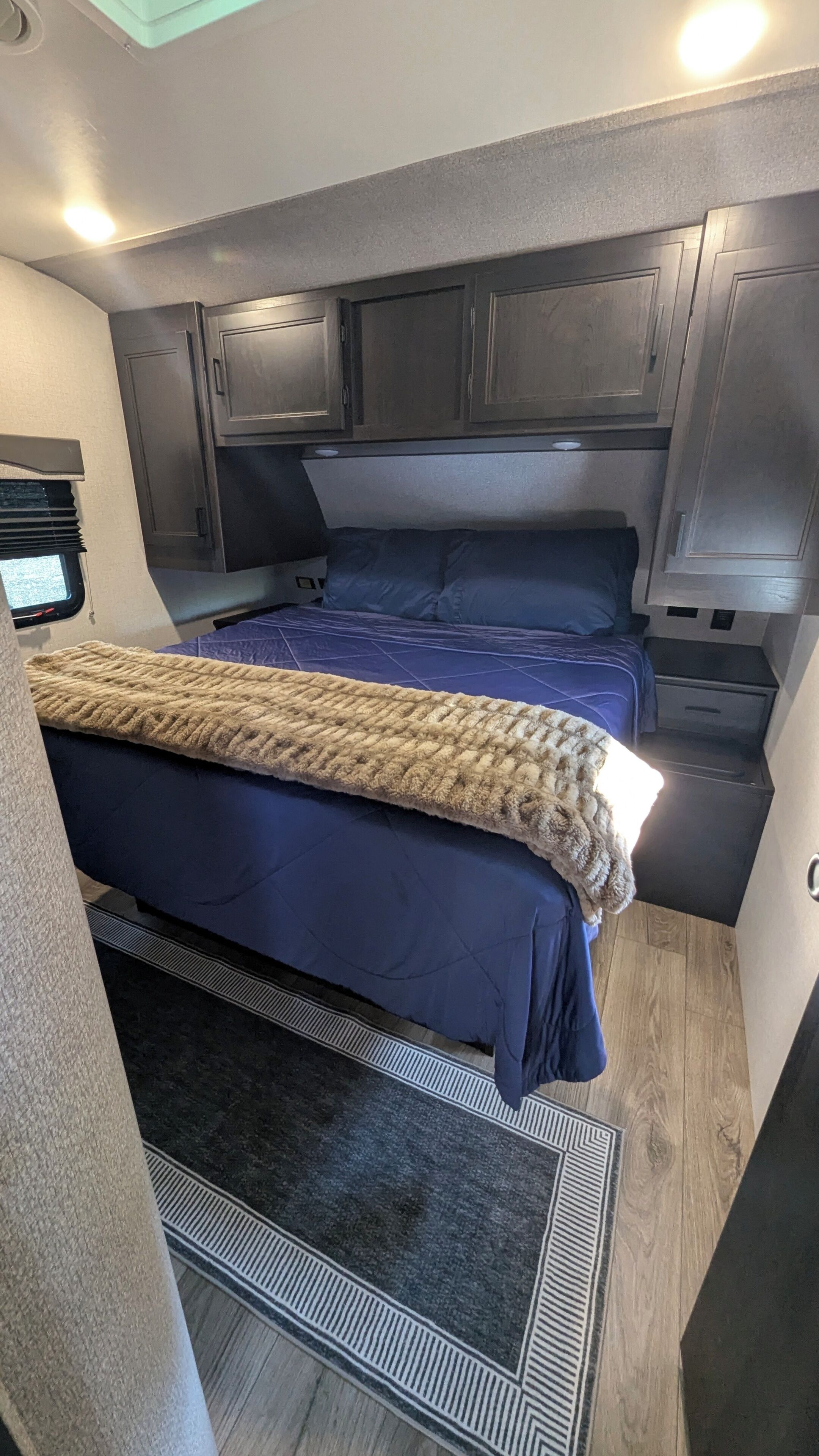 Interiør i en lille campingvogn med seng, tekøkken og et lille vindue.