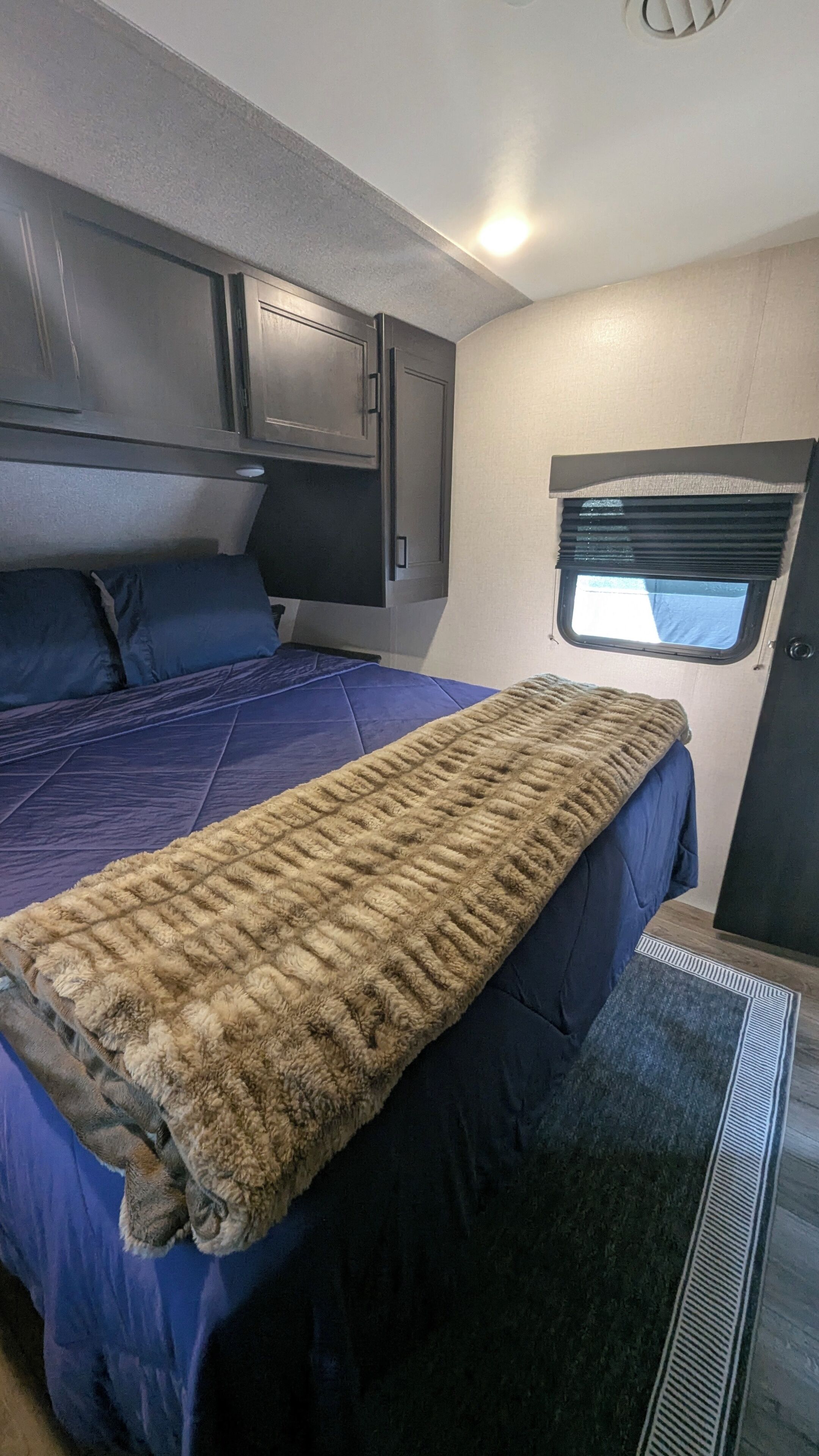 A compact RV interior with a bed, a window, and a kitchenette area.