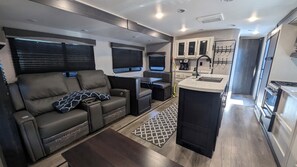 A compact RV interior with a sofa, kitchenette, and a small dining area. - RV Retreat on Green Thumb urban farm (Puyallup)