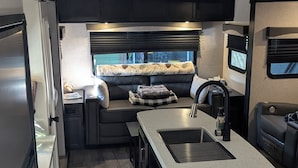 Une cuisine compacte pour camping-car, dotée d’un îlot central, d’appareils électroménagers intégrés et d’un coin salon offrant une vue agréable.