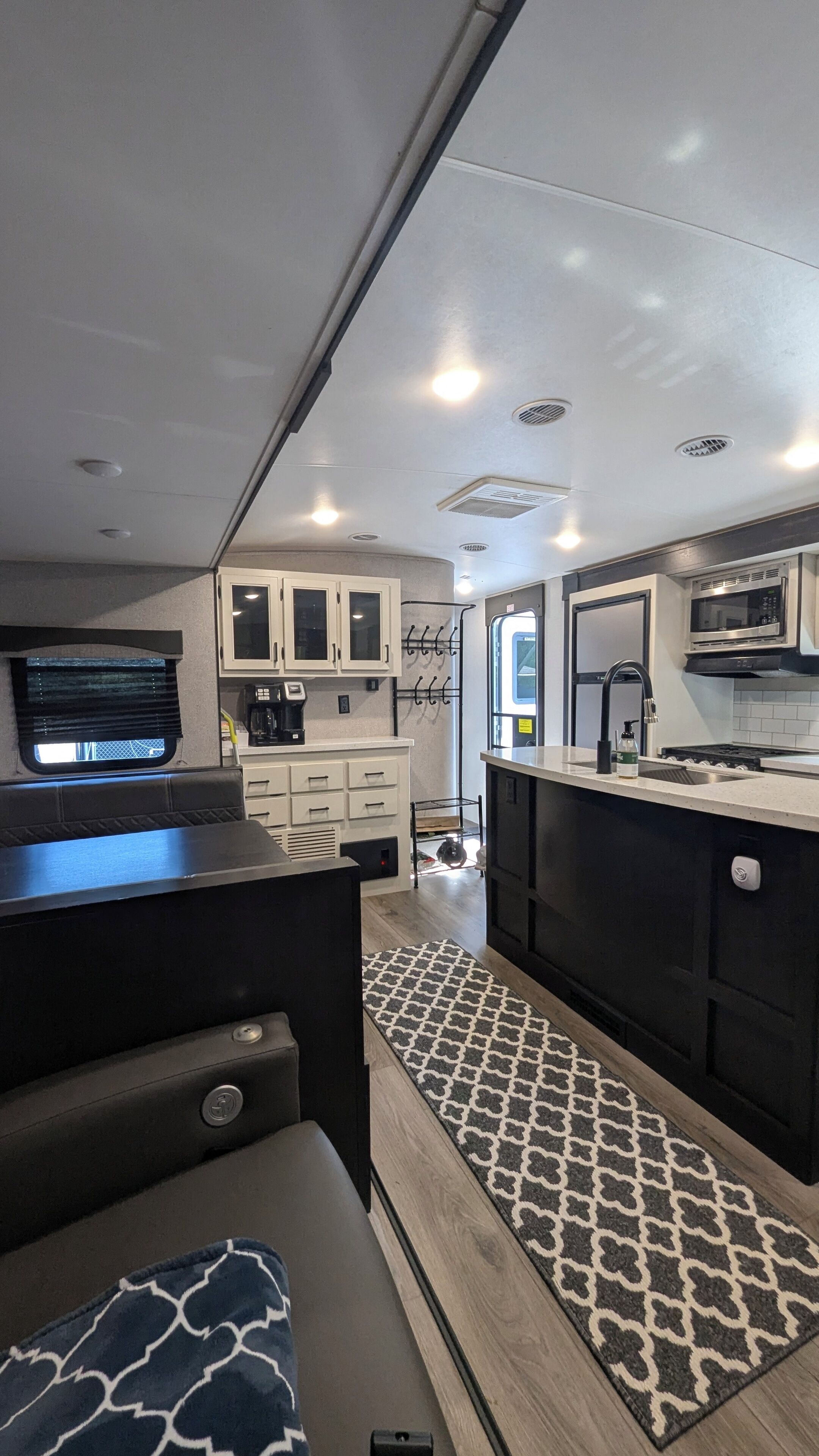 A compact RV kitchen with a dining area, white cabinets, a microwave, and a coffee maker.