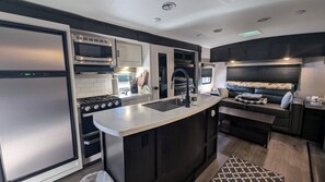 A compact kitchen with a microwave, stove, sink, and a small seating area with a couch. - RV Retreat on Green Thumb urban farm (Puyallup)