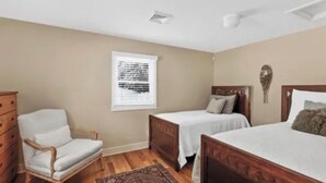 A bedroom with two single beds, a wooden dresser, a chair, and a window with blinds. - Elevate your Escape (Lake George)