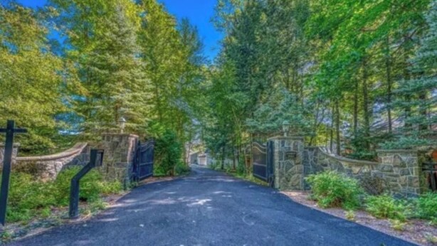 A paved driveway leading to a gated entrance surrounded by lush greenery and stone walls. - Elevate your Escape (Lake George)