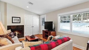 A cozy living room with a fireplace, a television, and a large window with a view of a snowy landscape. - Elevate your Escape (Lake George)