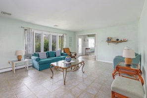 A spacious living room with a teal sofa, a glass coffee table, and a wicker chair. - Serenity and Water fun abound in. this 3+ Bedroom on the Lagoon in Bayville! (Berkeley Township)