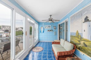A sunlit room with a blue tiled floor, a ceiling fan, a wicker sofa, and a large window overlooking a dock and boats. - Serenity and Water fun abound in. this 3+ Bedroom on the Lagoon in Bayville! (Berkeley Township)