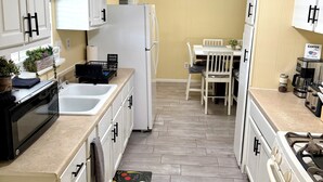 Una cocina con armarios blancos, un refrigerador, un microondas, un fregadero, una mesa de comedor con sillas y una estufa.