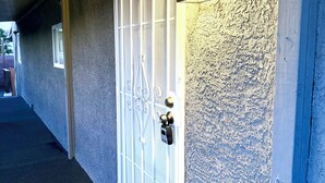 Un pasillo con una puerta metálica, un felpudo y una pared con textura.