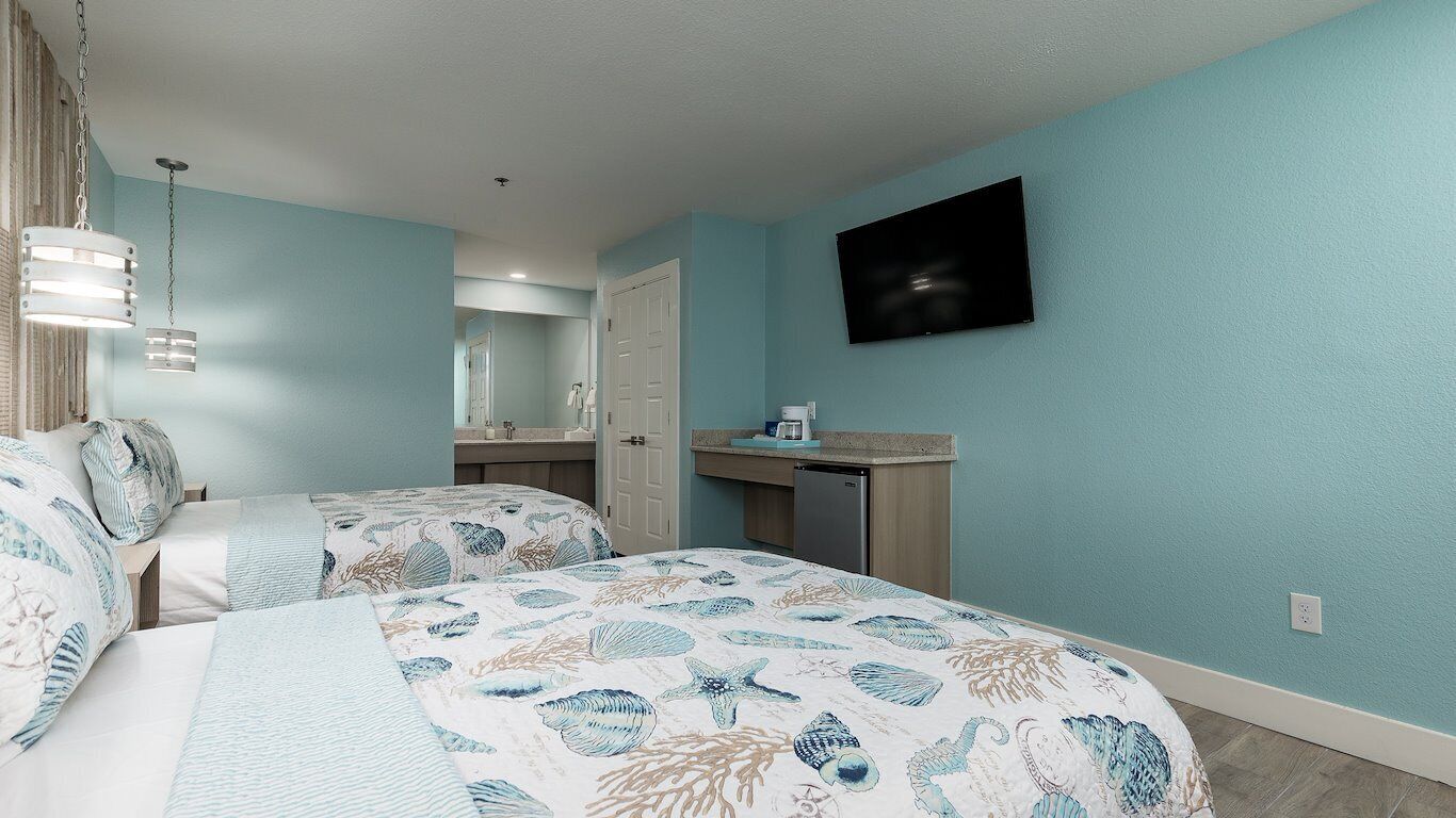 A bedroom with two beds, a TV mounted on the wall, and a bathroom visible through an open door.
