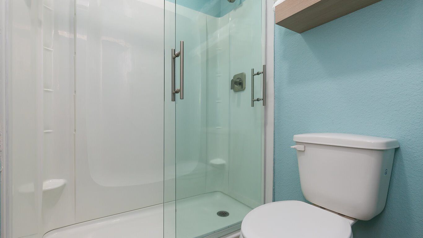 A bathroom with a glass-enclosed shower, a white toilet, and a light blue wall.