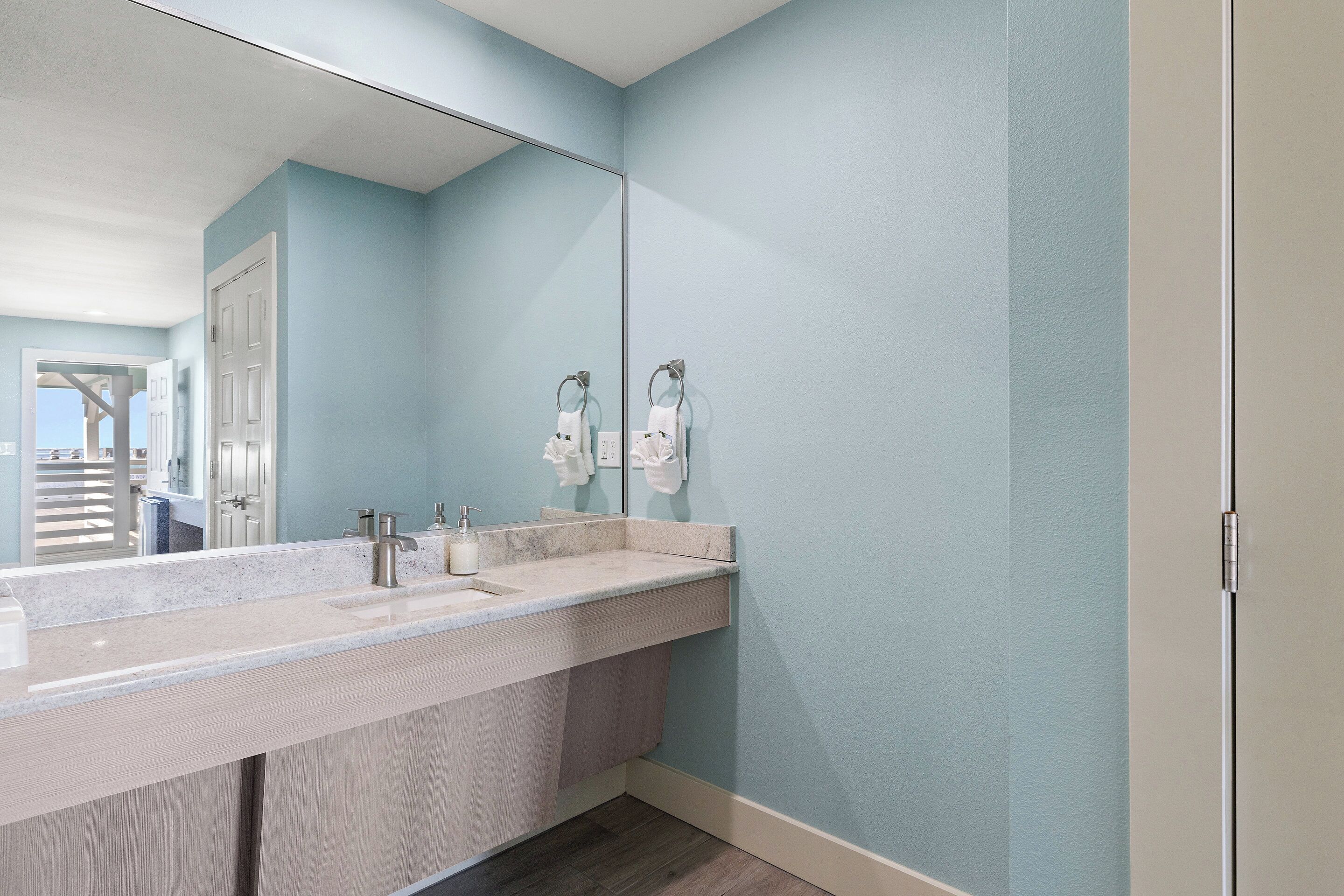 A bathroom with a large mirror, a sink with a marble countertop, and a towel rack.