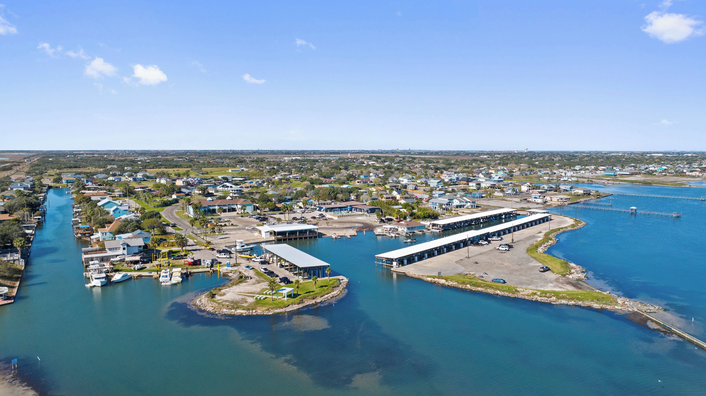 An aerial view of a coastal town with a marina, houses, and a large body of water.