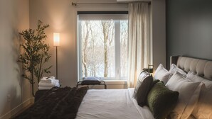 A hotel room with a large bed, a bedside table, a floor lamp, and a window with curtains.