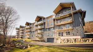 A multi-story residential building with balconies, a stone facade, and a grassy driveway.