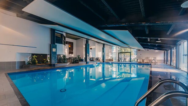 An indoor swimming pool with clear glass walls, a tiled floor, and a metal ladder.