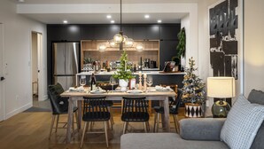 A modern kitchen with dark cabinetry, a central island, and a dining area with a chandelier.