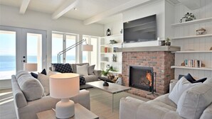 Una sala de estar moderna con chimenea, ventanas amplias y vista al océano.