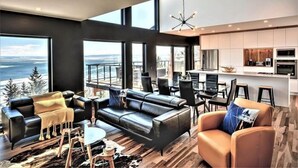 Un salon moderne avec un grand canapé en cuir noir, une table basse et une vue sur l’océan.
