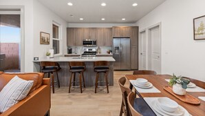 A modern kitchen with a central island, bar stools, and a dining area with a wooden table and chairs. - New- Pool, Hot Tub, Nintendo Switch, Pool, Pickleball and Ping Pong Fun (Santa Clara)