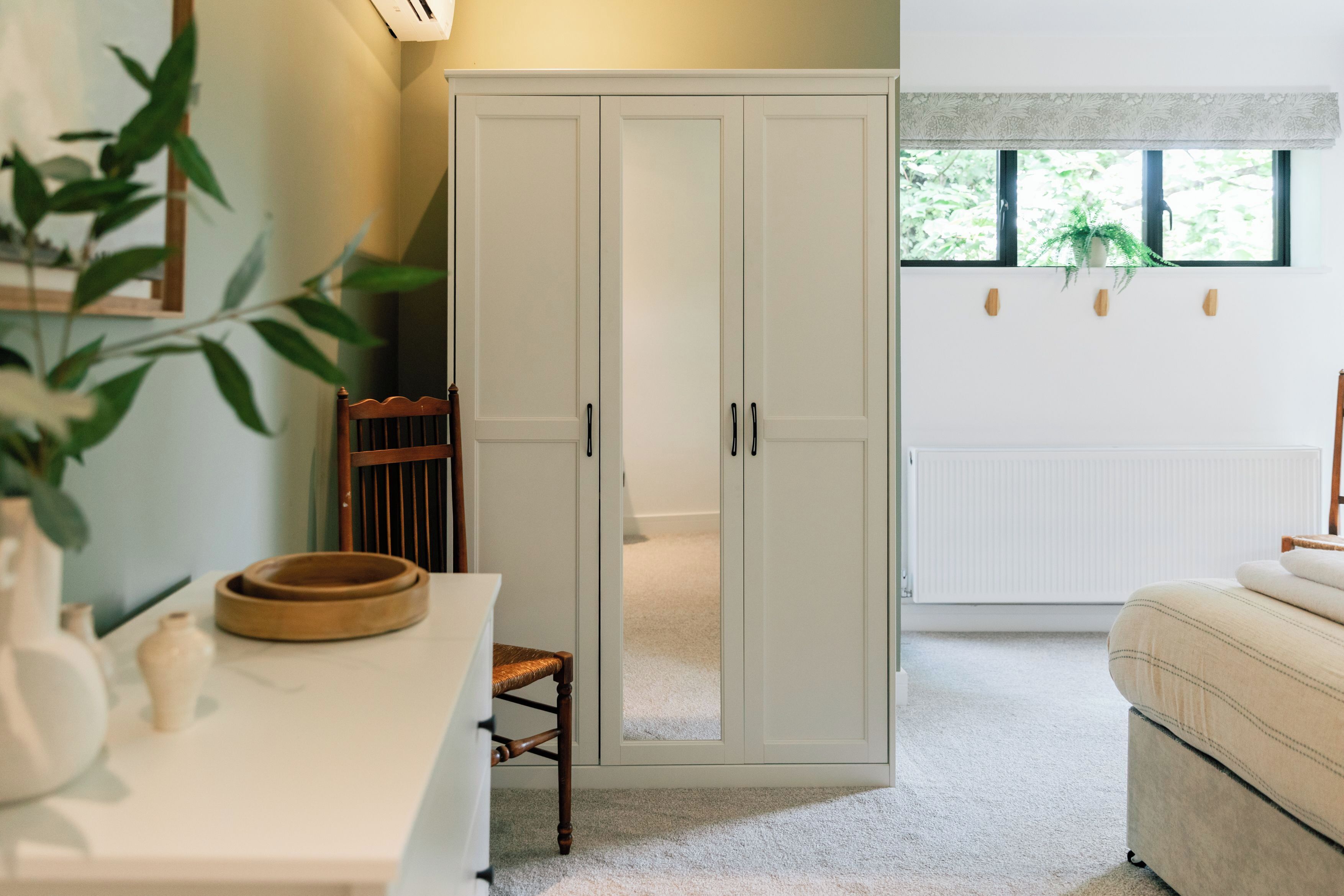 A room with a white wardrobe, a wooden chair, a small table with a bowl, and a bed.