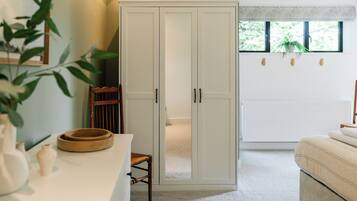 A room with a white wardrobe, a wooden chair, a small table with a bowl, and a bed.