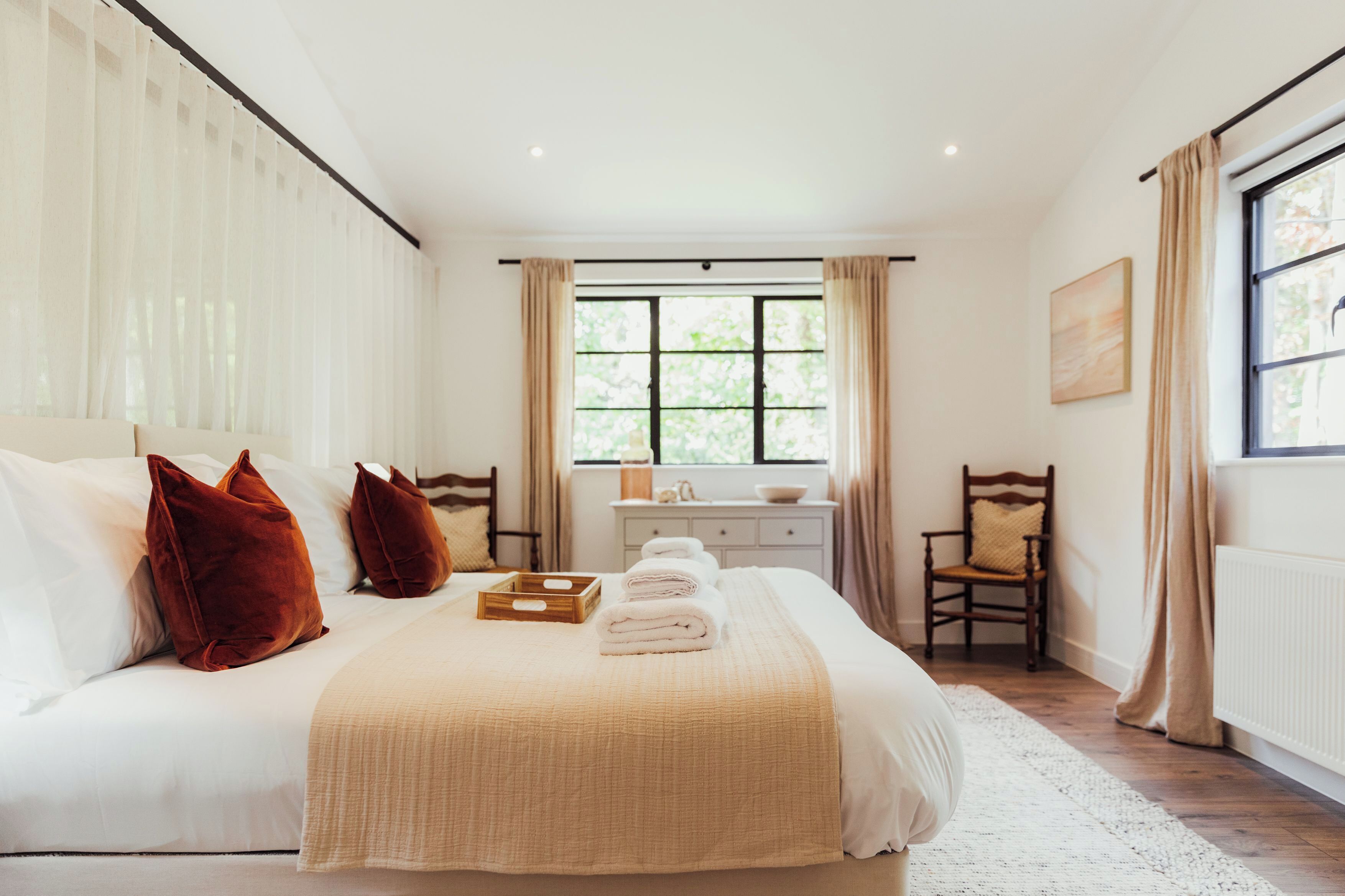 A bedroom with a large bed, a bedside table, a chair, and a window with curtains.