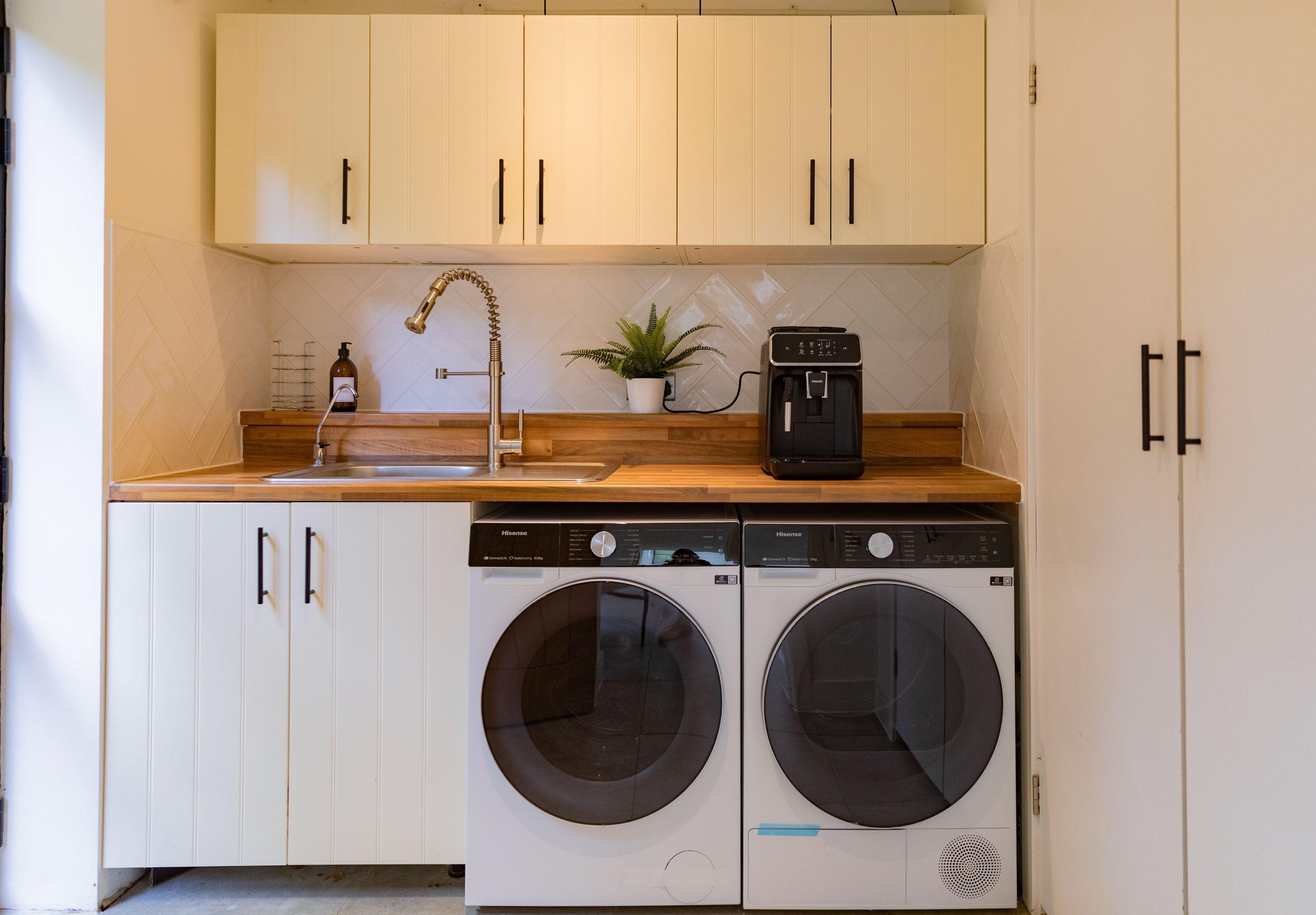 A compact kitchen with two front-loading washing machines, a coffee maker, and a potted plant.