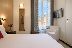 A hotel room with a bed, a chair, a TV mounted on the wall, a decorative wall hanging, and a window with curtains. - Gli Scipioni Bed & Breakfast (Rome)