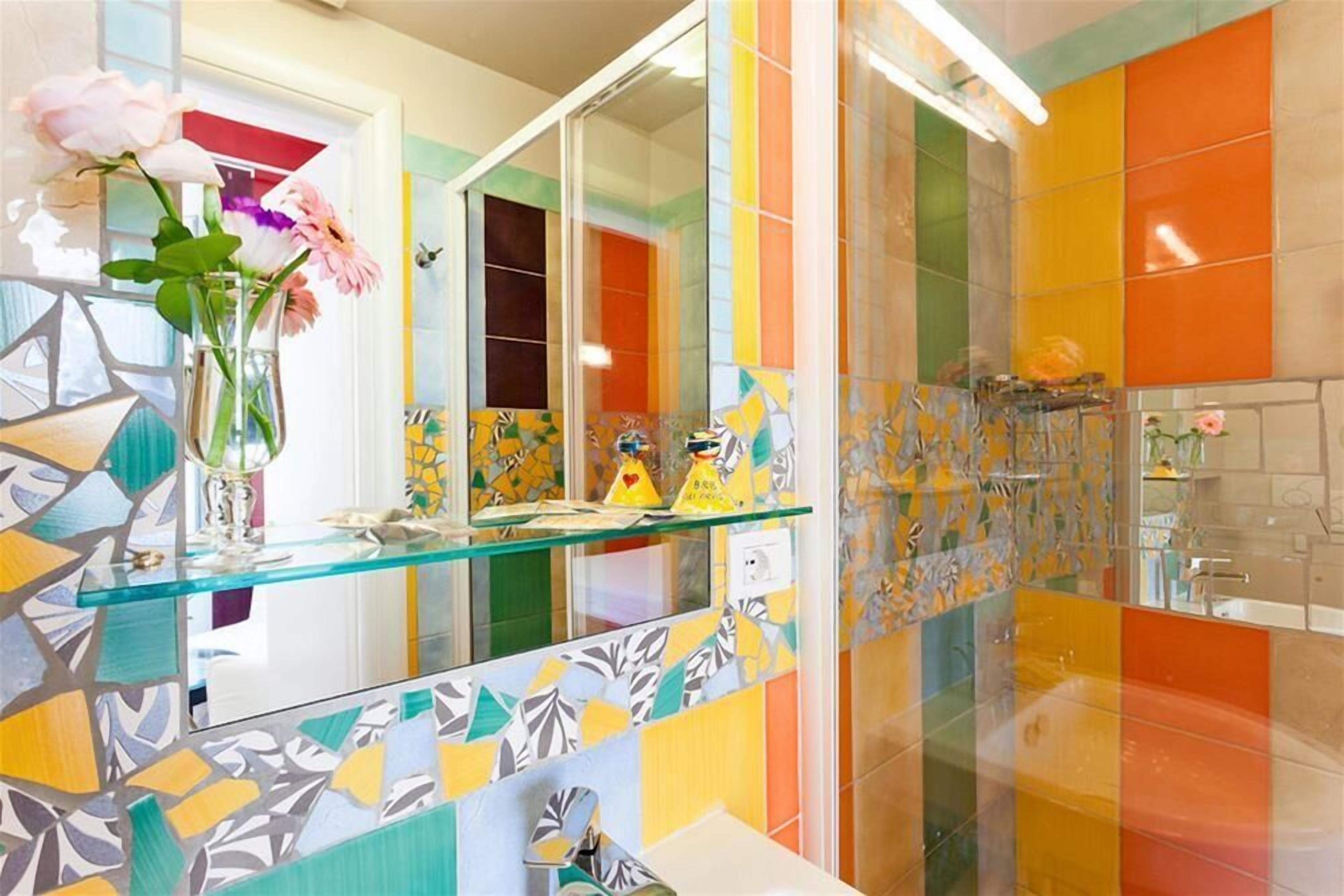 Un baño con tocador de vidrio, azulejos coloridos y un espejo.