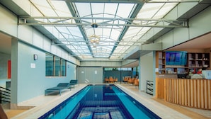 Piscina interna com teto de vidro, área de estar e balcão de recepção.