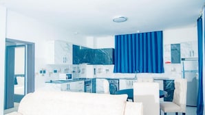 Uma cozinha moderna com bancadas de mármore e cortinas azuis, uma área de refeições com sofá branco e um banheiro visível.