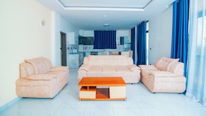 Uma sala de estar moderna com um sofá, uma mesa de centro de madeira e uma cozinha ao fundo.