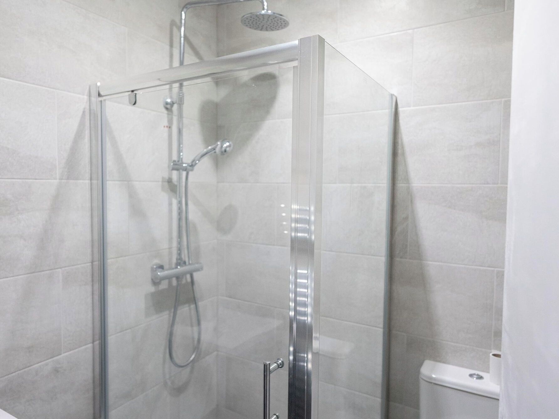 A glass-enclosed shower stall with a handheld showerhead and a wall-mounted faucet.