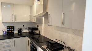 A modern kitchen with white cabinets, a black countertop, a built-in microwave, a toaster, a kettle, and a washing machine.