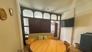 A dining area with a round wooden table and chairs, a sofa, and a TV mounted on the wall. - Rent Up -Monoambiente en zona tribunales (Buenos Aires)