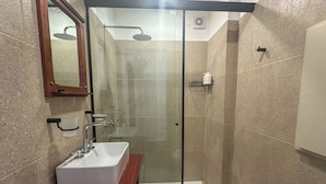 A modern bathroom with a glass-enclosed shower, a white sink, and a wooden vanity. - Rent Up -Monoambiente en zona tribunales (Buenos Aires)