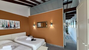 Ein Hotelzimmer mit zwei Betten, einem Segelbootbild, Wandleuchten und einem Blickgang.