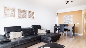 A modern living room with a black leather sofa, a dining table with chairs, and decorative wall art.