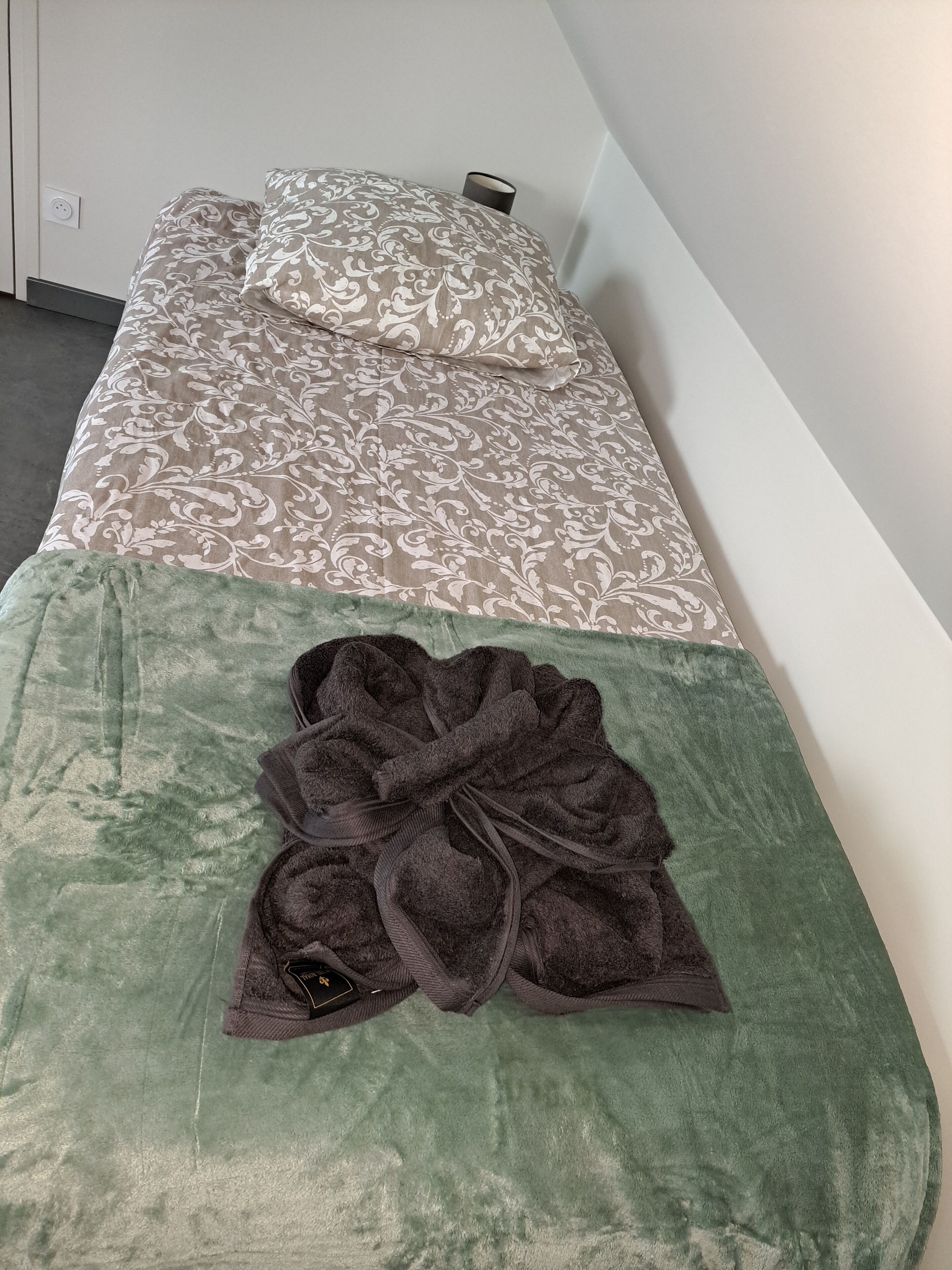 Un lit simple avec une couvre-lit à motifs et une serviette verte posée sur le bord inférieur.
